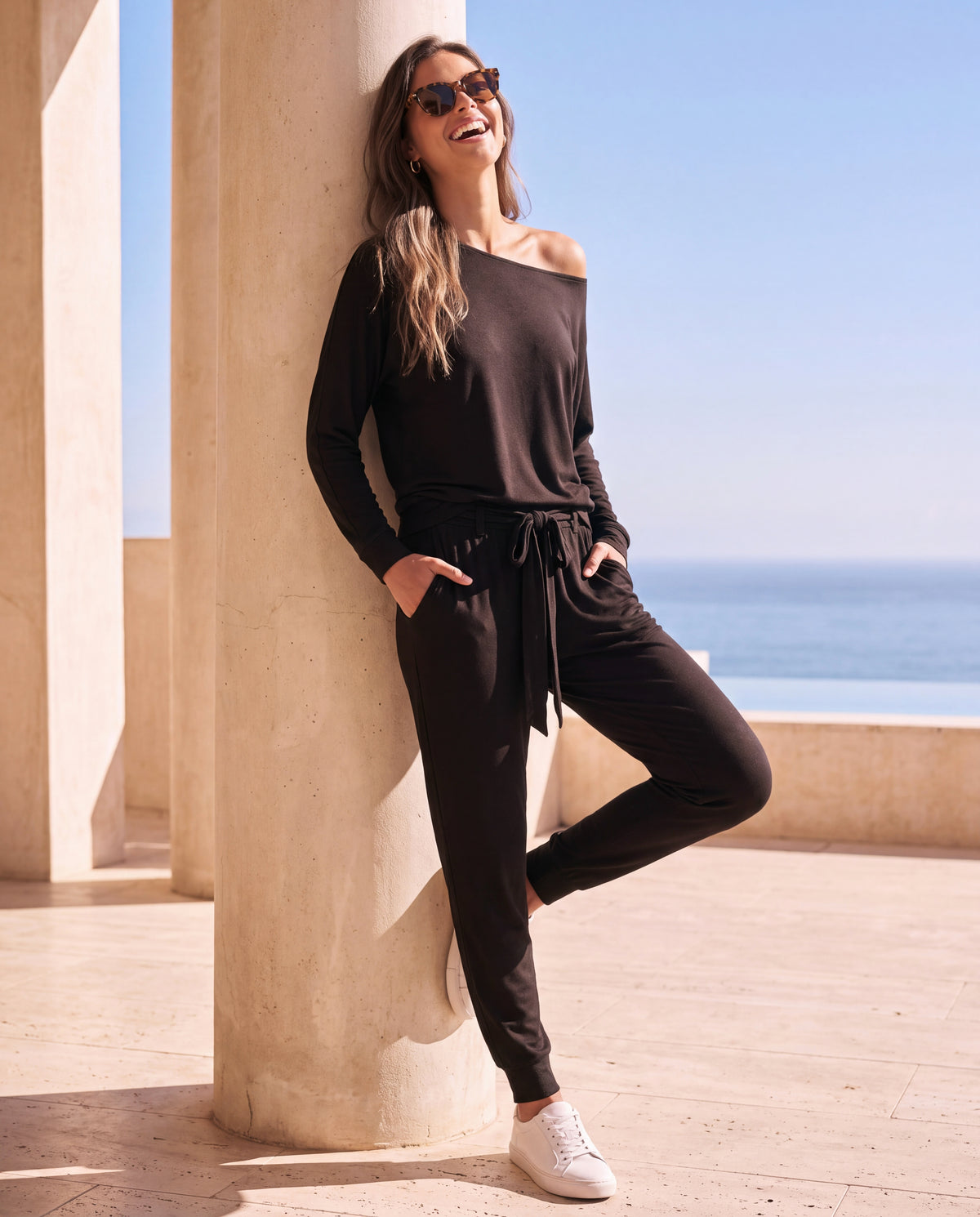 The Willow Lounge Set in Coal, leaning on a column with a sea view