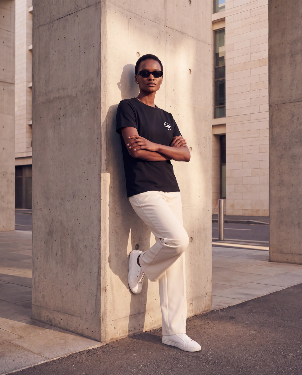 The Signature Tee in Black, leaning on concrete column